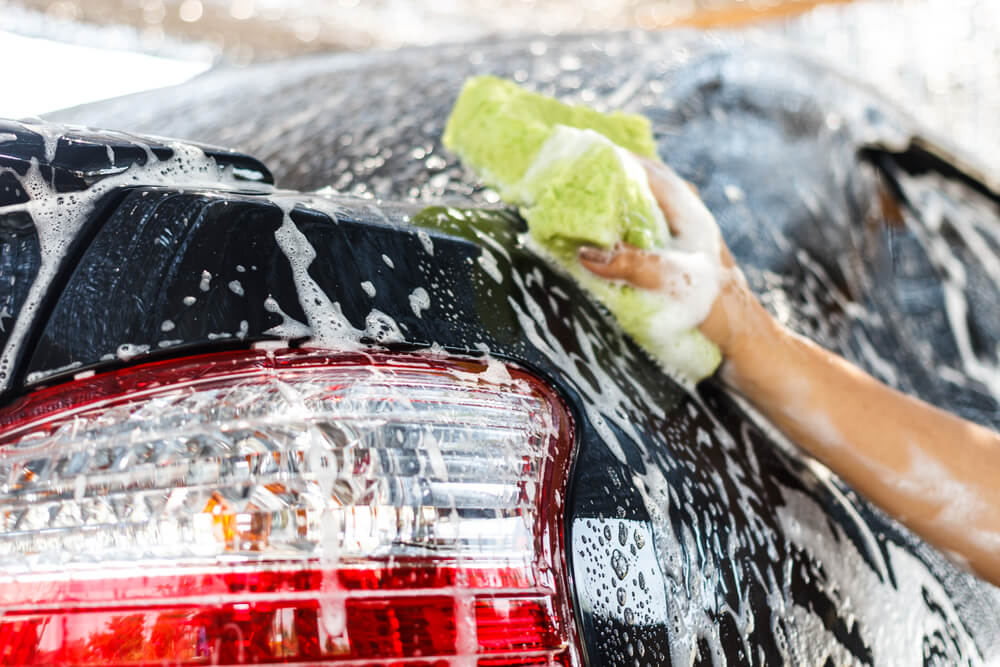 スポンジに泡を付けて洗車をする男性の手